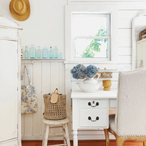 Vintage pieces of white wooden furniture featuring a ledge of light blue glass bottle collection.