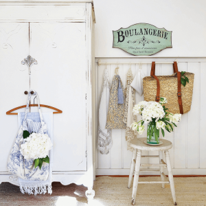 White wooden rustic wardrobe, jute rug and a flowers perched atop a wooden stool.