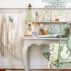Minty green hand-painted chair with a custom made pom-fringed pillow in front of a wooden desk.
