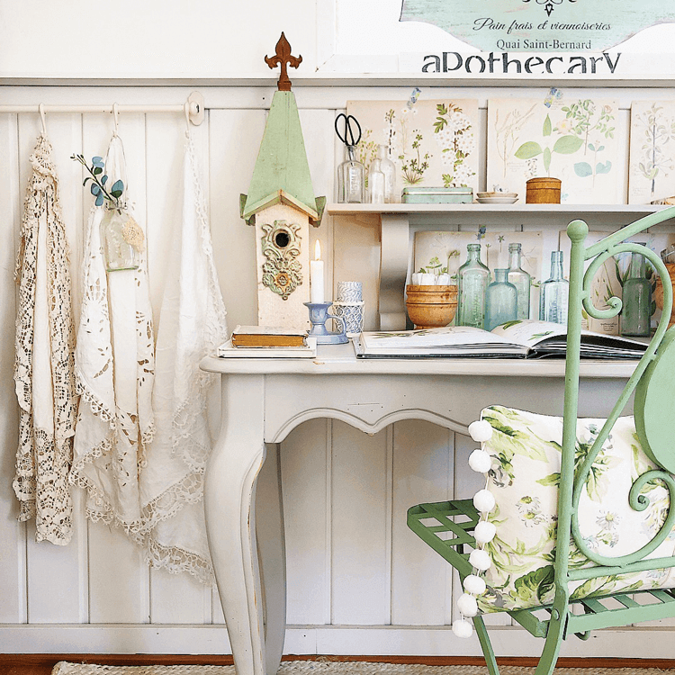 a white carved wood desk is topped with old books and garden decor