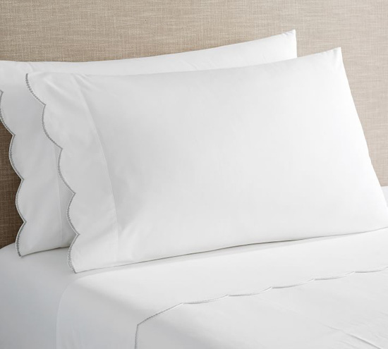 White sheets with a scalloped edge featured on a bed and pillows.