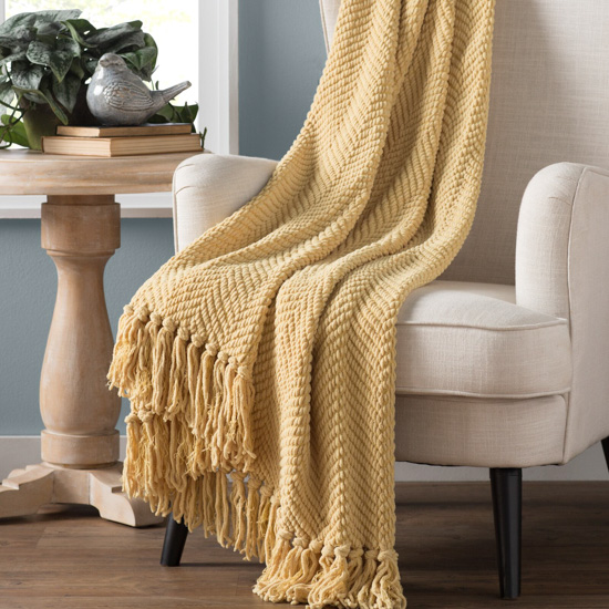 Oatmeal colored armchair with light mustard colored throw blanket draped over the top. 