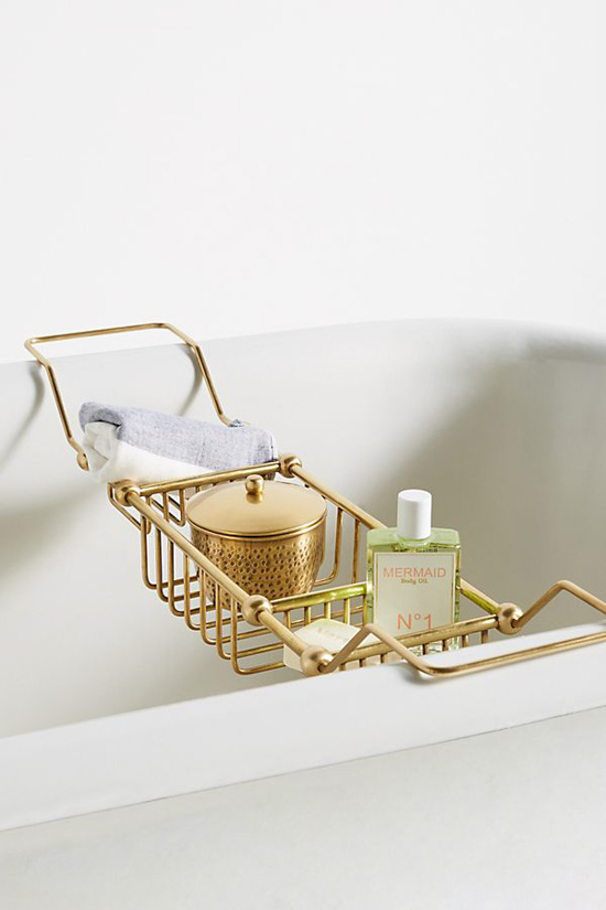 Gold, metal bath caddy perched on a bathtub and filled with shower products. 