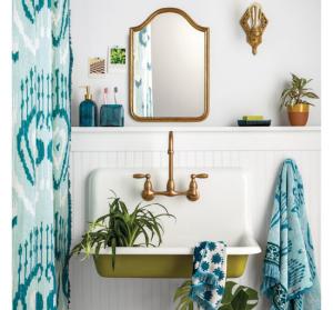 Funky cottage bathroom, all white with pops of green and blue, showing shower curtain., mirror, sink, house plants and patterned towels.
