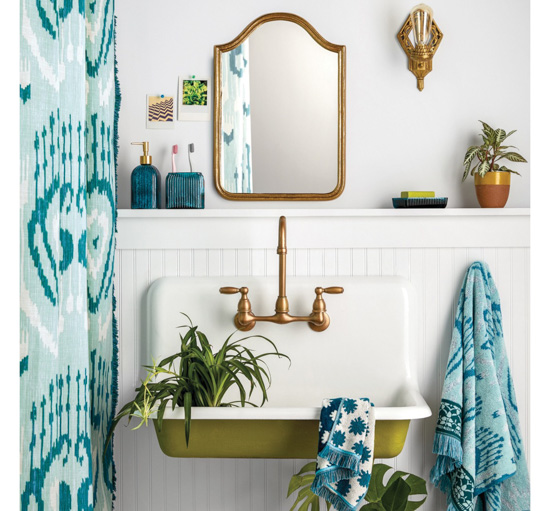 Funky cottage bathroom, all white with pops of green and blue, showing shower curtain., mirror, sink, house plants and patterned towels. 