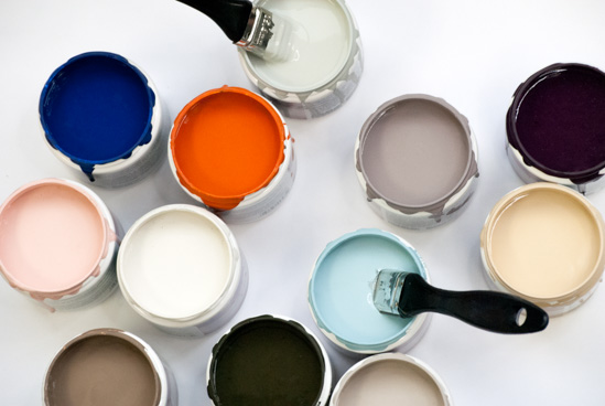 Open paint cans of various colors with one paintbrush sticking out of a can. 