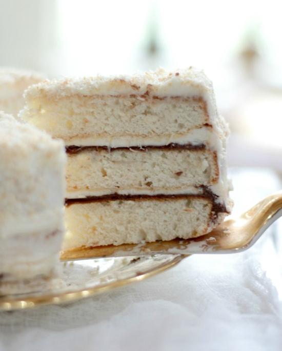 Slice of three layered white cake with Nutella layered filling being pulled out on a spatula. 