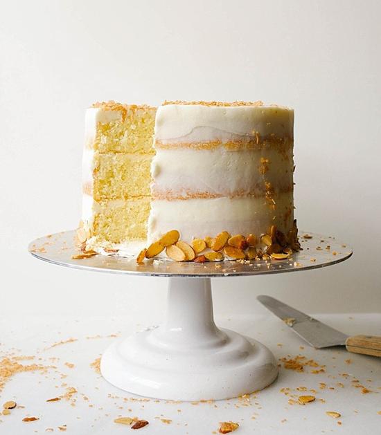 white cake stand with a three layered cake on top with a slice missing and a spatula laying on the table next to it.