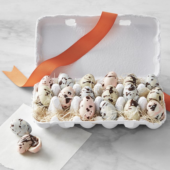 Cardboard egg crate filled with speckled candy eggs on a marble countertop. 