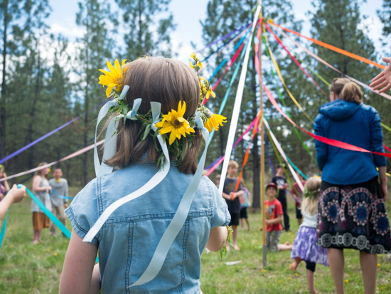 Children dancing around a May Pole holding colorful ribbons.