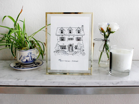 Ink on paper drawing of a custom house in a gold frame on a marble counter top.