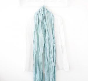 Organic cotton light blue scarf hanging on a white wall under a hat.