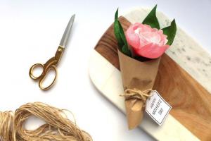 Hand made paper flower wrapped in brown paper laying on a cutting board next to scissors and twine.