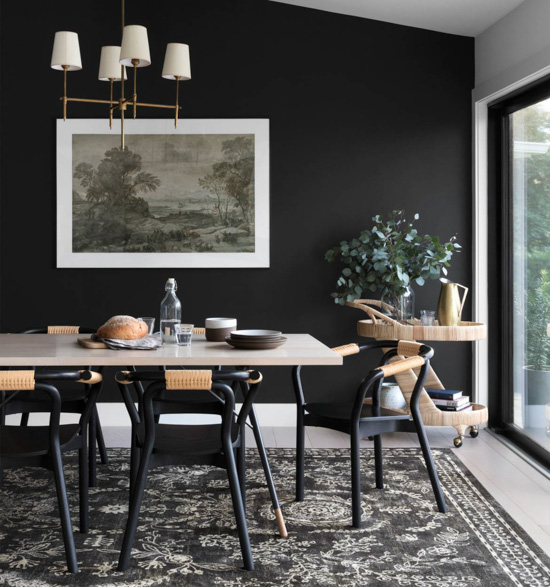 Modern dining room with large windowed wall and black back wall featuring a Rifle Paper Co. rug under the dining table.