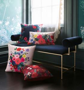 Rifle Paper Co.'s new pillow collection displayed on a navy blue and gold accented bench.