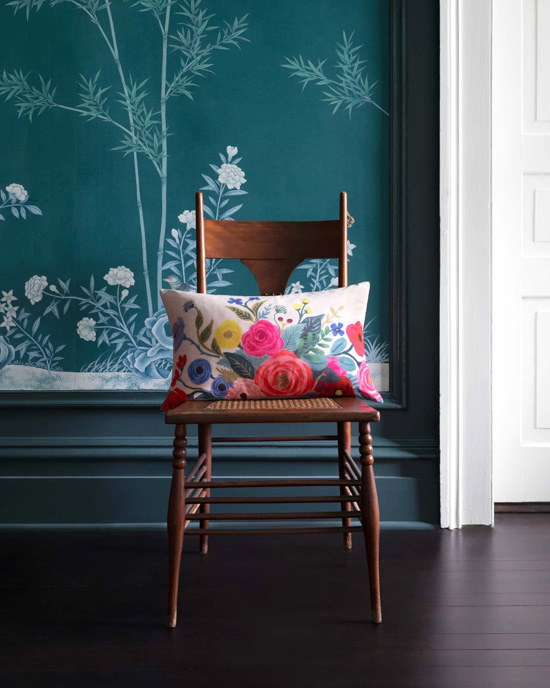 Wallapered wall with a wooden chair in front of it displaying a floral lumbar pillow.