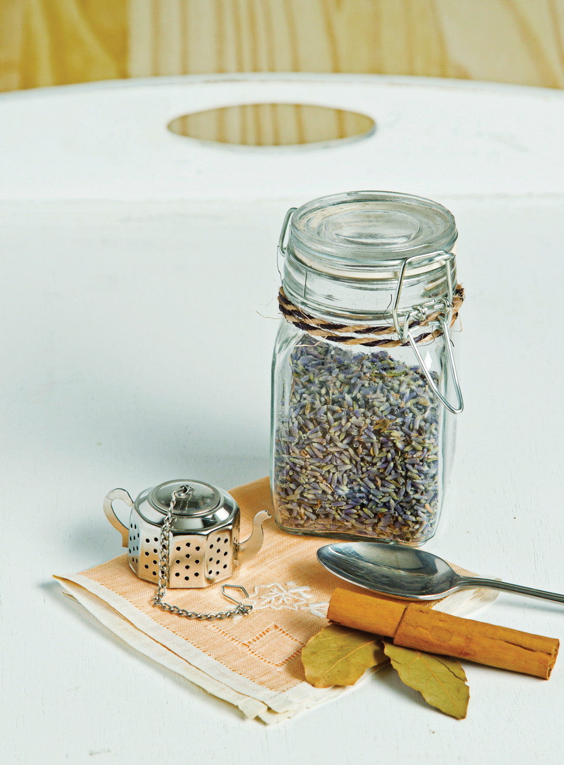 Metal teapot shaped tea diffuser, cinnamon stick, spoon, glass canister filled with lavender. 