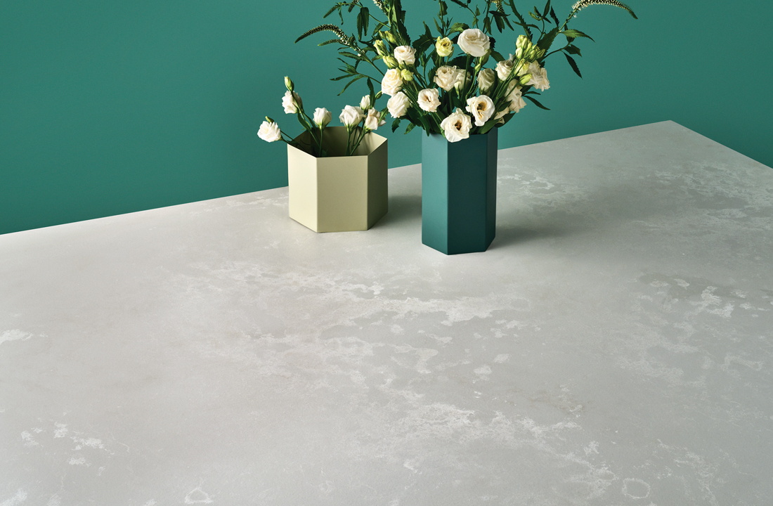 Modern looking concrete countertops with angular vases filled with fresh florals and a teal painted wall in the background.