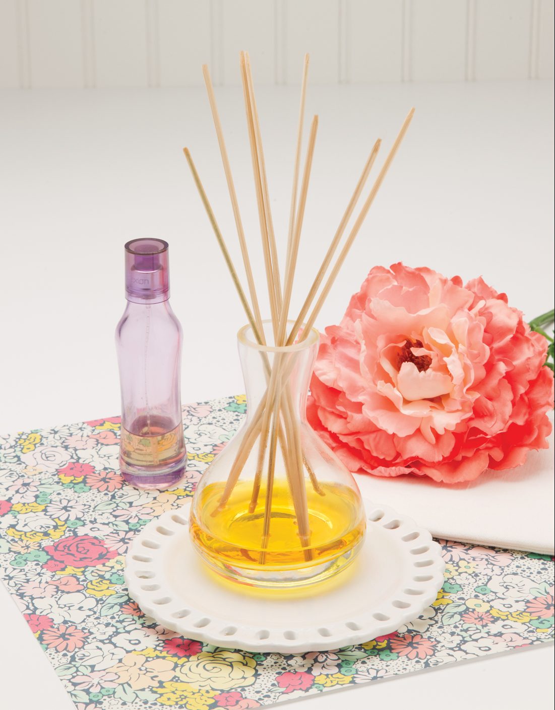 Beautifully displayed reed diffuser with light and bright colors and a coral colored rose. 