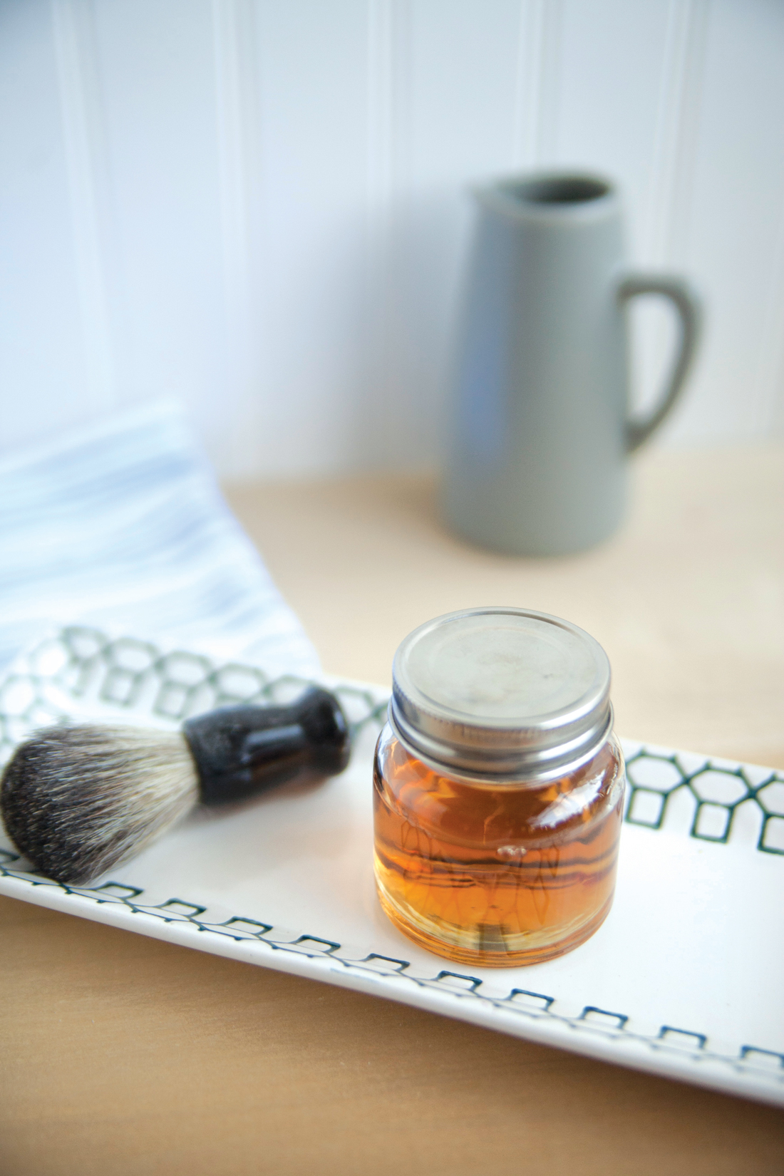 Facial brush and glass jar of golden colored beard oil. 