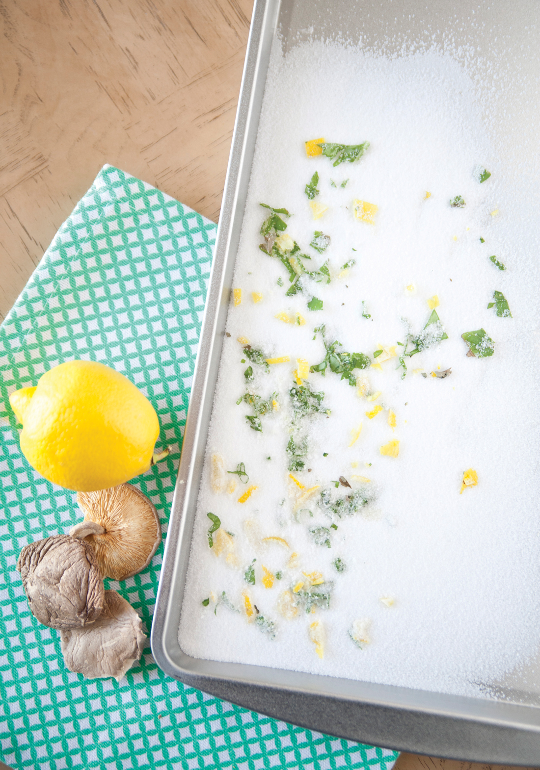 Baking sheet covered in salt, lemon zest and mushrooms pieces displayed next to lemons and porcini mushrooms. 