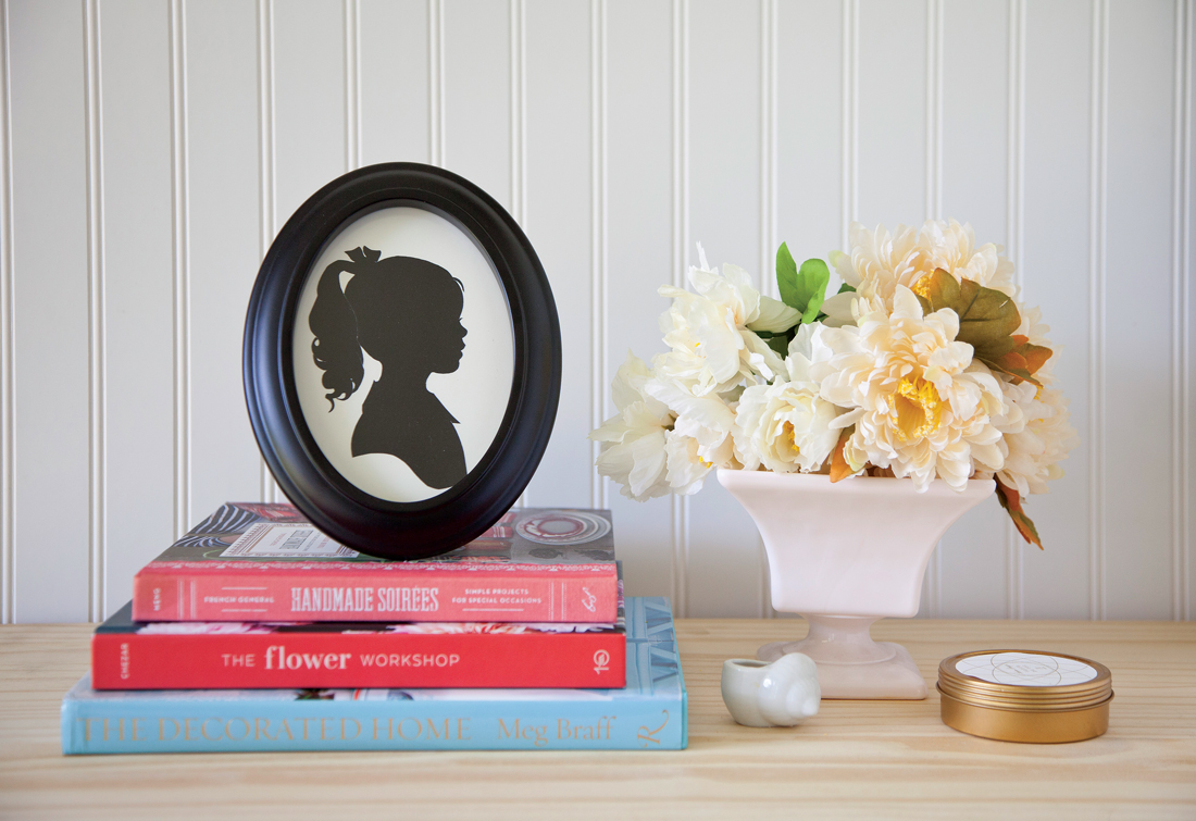 Custom oval framed silhouette placed on stacked books next to a vase of flowers.