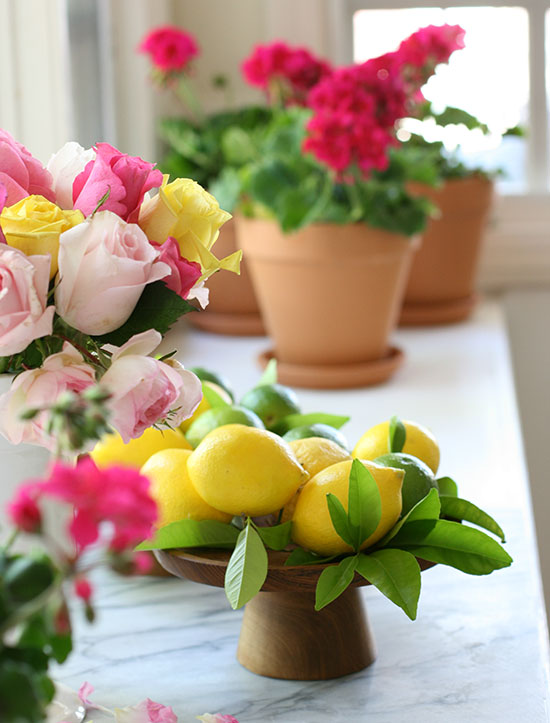 a wooden pedestal full of lemons and potted gernaniums in the background