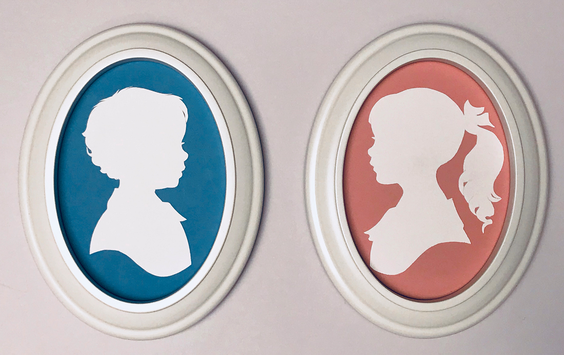 Custom portraits of a boy and a girl in white oval frames with the silhouettes facing each other hanging on the wall. 