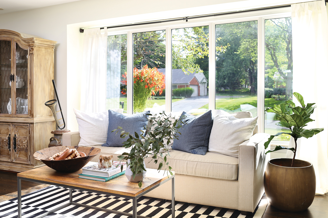 Striped rug with a cream colored cozy couch in front of a huge bright window. 