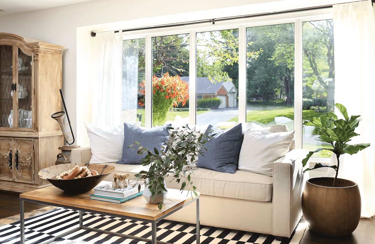 Striped rug with a cream colored cozy couch in front of a huge bright window.