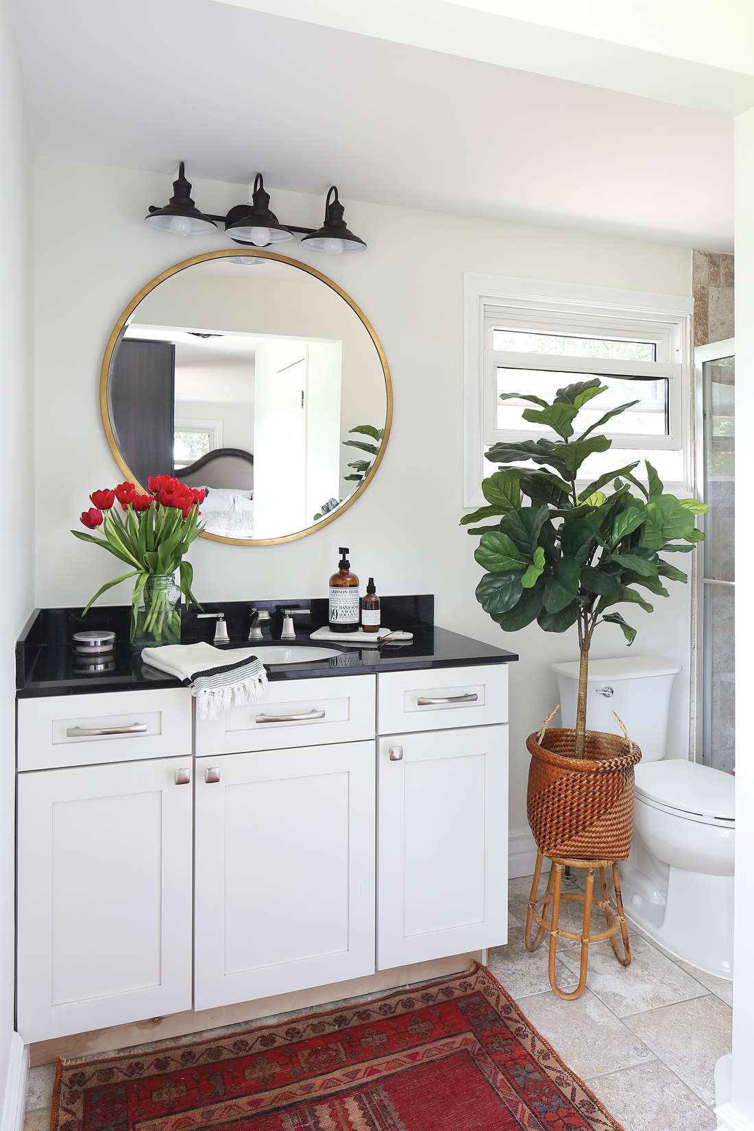 Master bathroom with vintage rug, modern round mirror and a stylish fiddle leaf fig tree. 