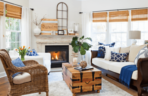 Spacious living room with light gray/beige walls, wicker and wooden rustic furniture accent pieces and pops of blue in pillows and throws.