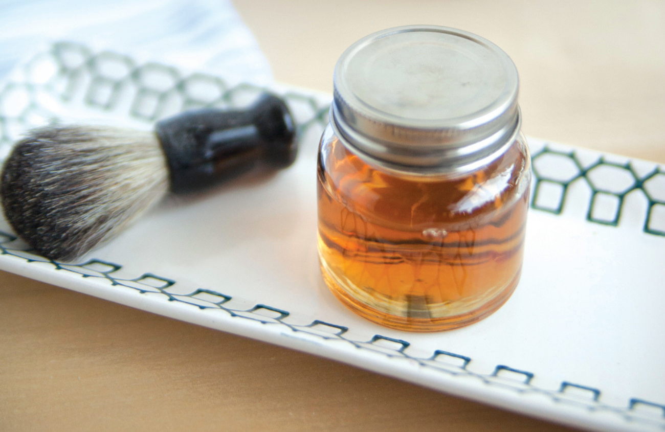 Facial brush and glass jar of golden colored beard oil.