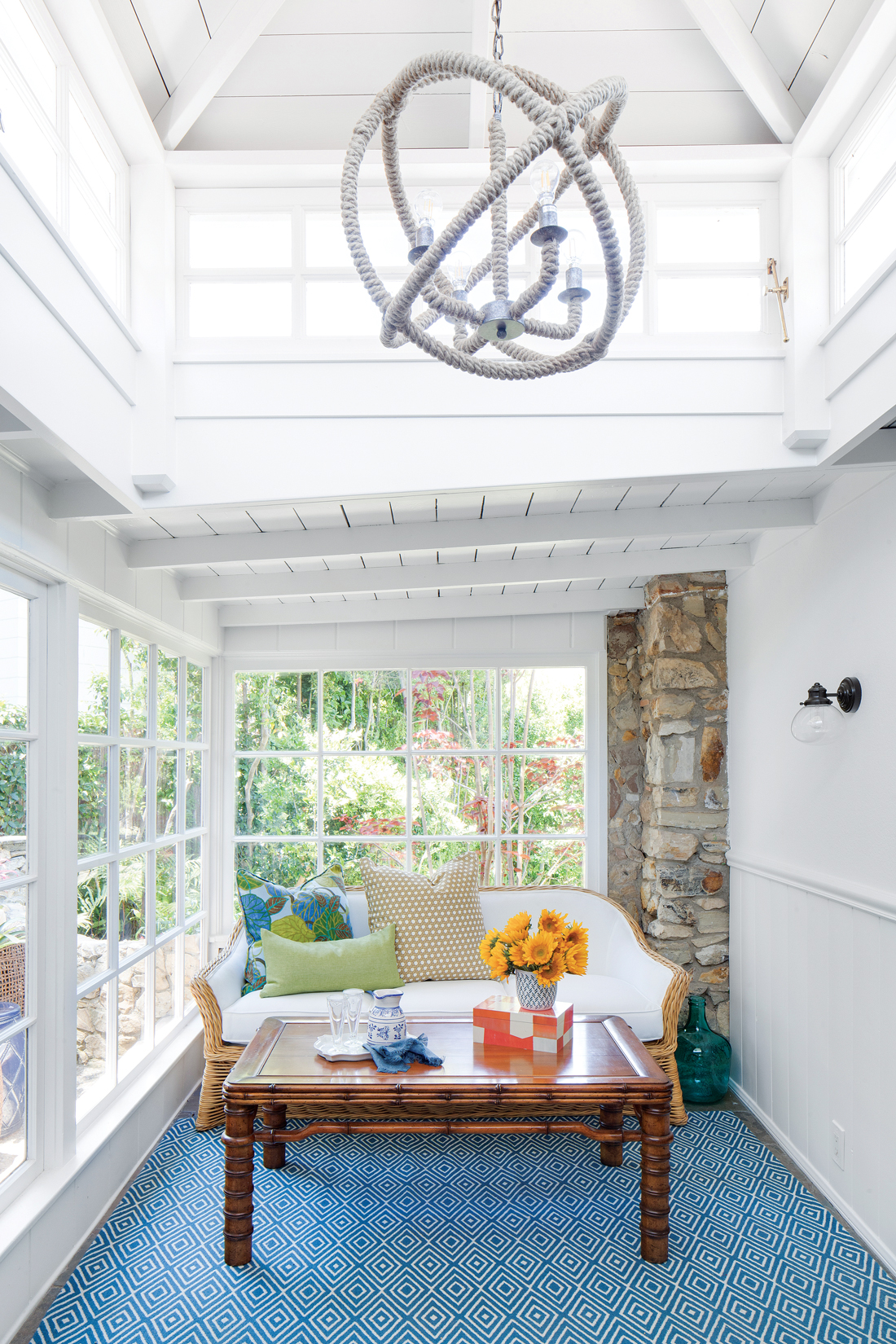 Sun room in a cottage beach house with a white nautical rope light fixture hanging from the vaulted ceiling over a seating area. 