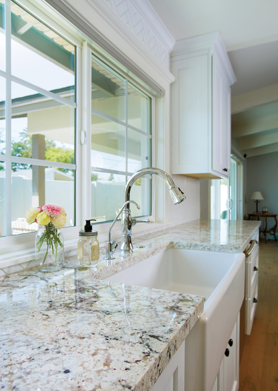 Natural stone granite countertop in a white cabinet kitchen with a farmhouse sink and roses in a glass vase on the counter. 