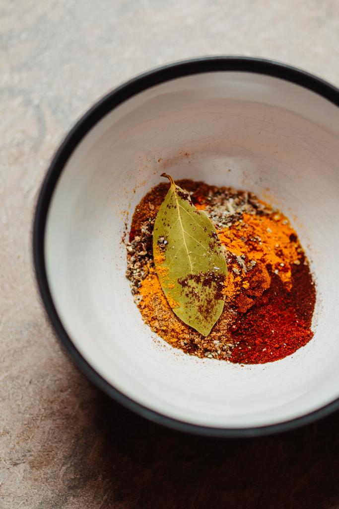 Bowl filled with brightly colored seasonings and a bay leaf.