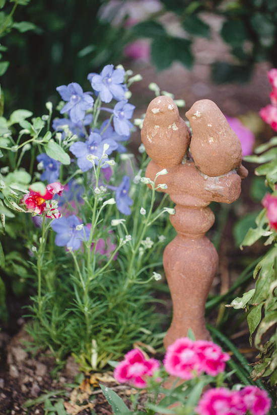 Stone bird statue amongst bright colored flowers.