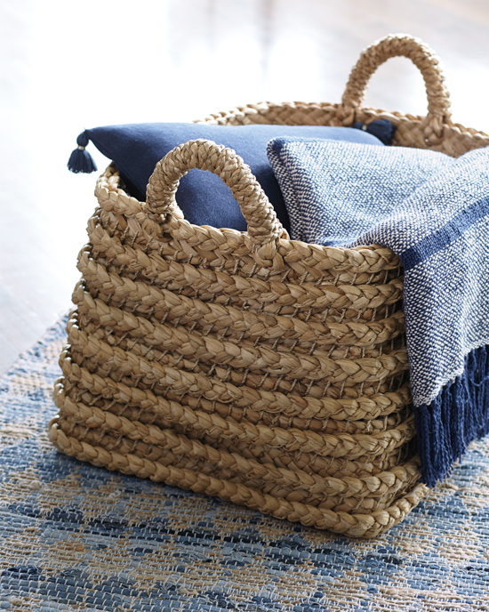 Whicker basket with handles displayed holding a blue pillow and similar colored throw blanket