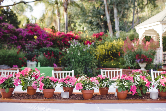 Tablescape on an outdoor seating area topped with pink and white florals in terra-cotta pots. 