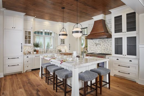 Modern cottage kitchen with brass range hood and orb pendant lights. 