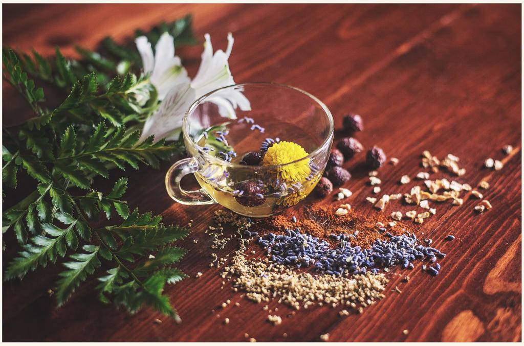 A small glass teacup filled with and surrounded by tea ingredients on a wooden table. 