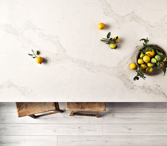 wooden barstools peaking out from under a marble countertop with a bowl of citrus adding color to the countertop.