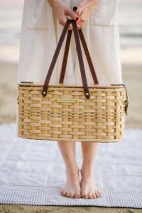 Girl standing on the beach in a light colored dress holding a picnic basket.