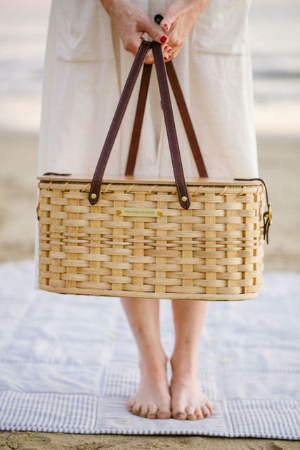 Girl standing on the beach in a light colored dress holding a picnic basket. 