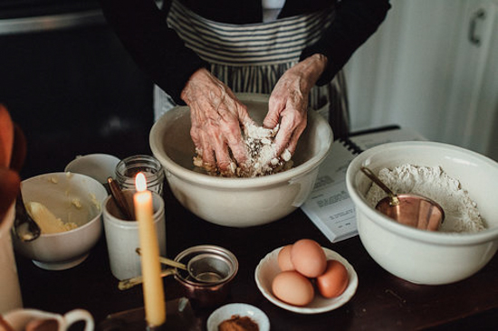 A cluttered table covered in baking supplies and an old woman's hands kneading dough.