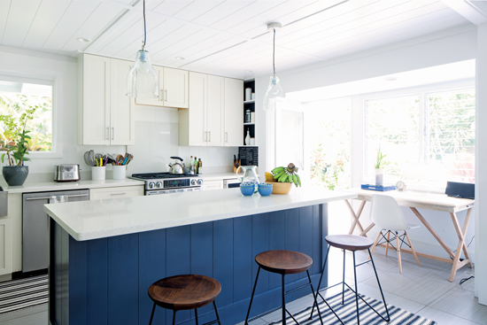 Bright and white kitchen with white quartz countertops and a navy blue paneled island. 