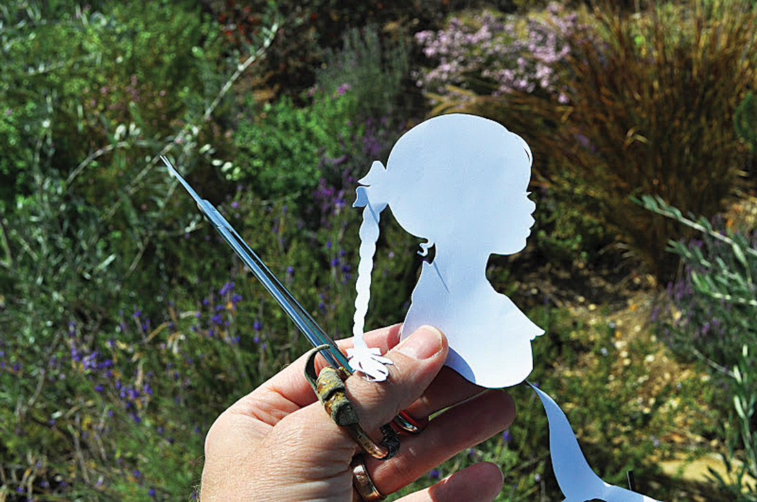 Hand holding scissors and cutting a custom silhouette of young girl with a long braid. 