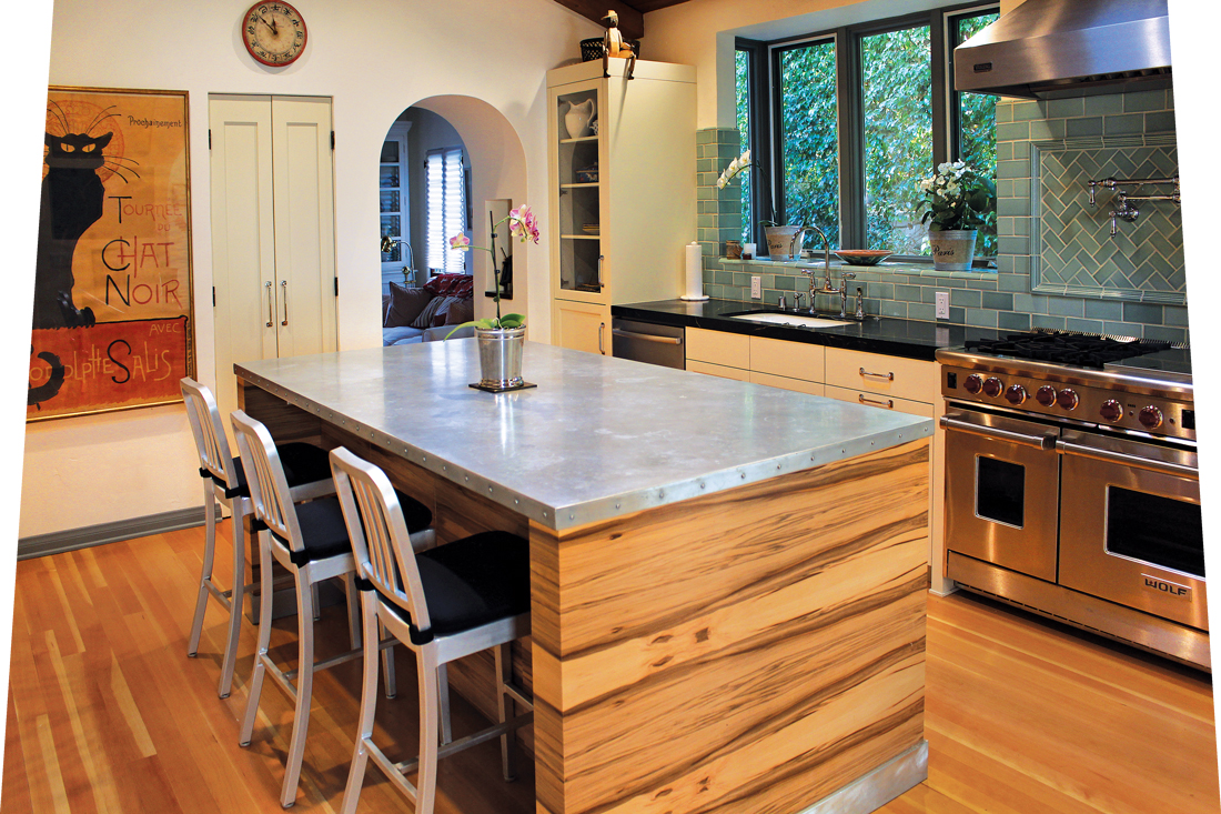 Wooden island with modern silver, zinc countertops with an industrial range in view.