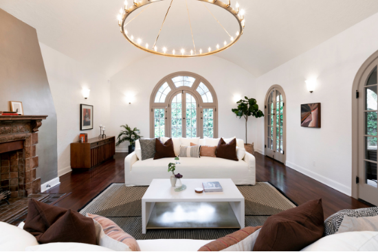 A farmhouse-style chandelier hangs over a modern white table and couches with dark neutral throw pillows.