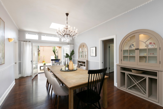 A beautiful chandelier hangs over a dining table with mismatched chairs and colorful plates pop from behind the china cabinet glass.